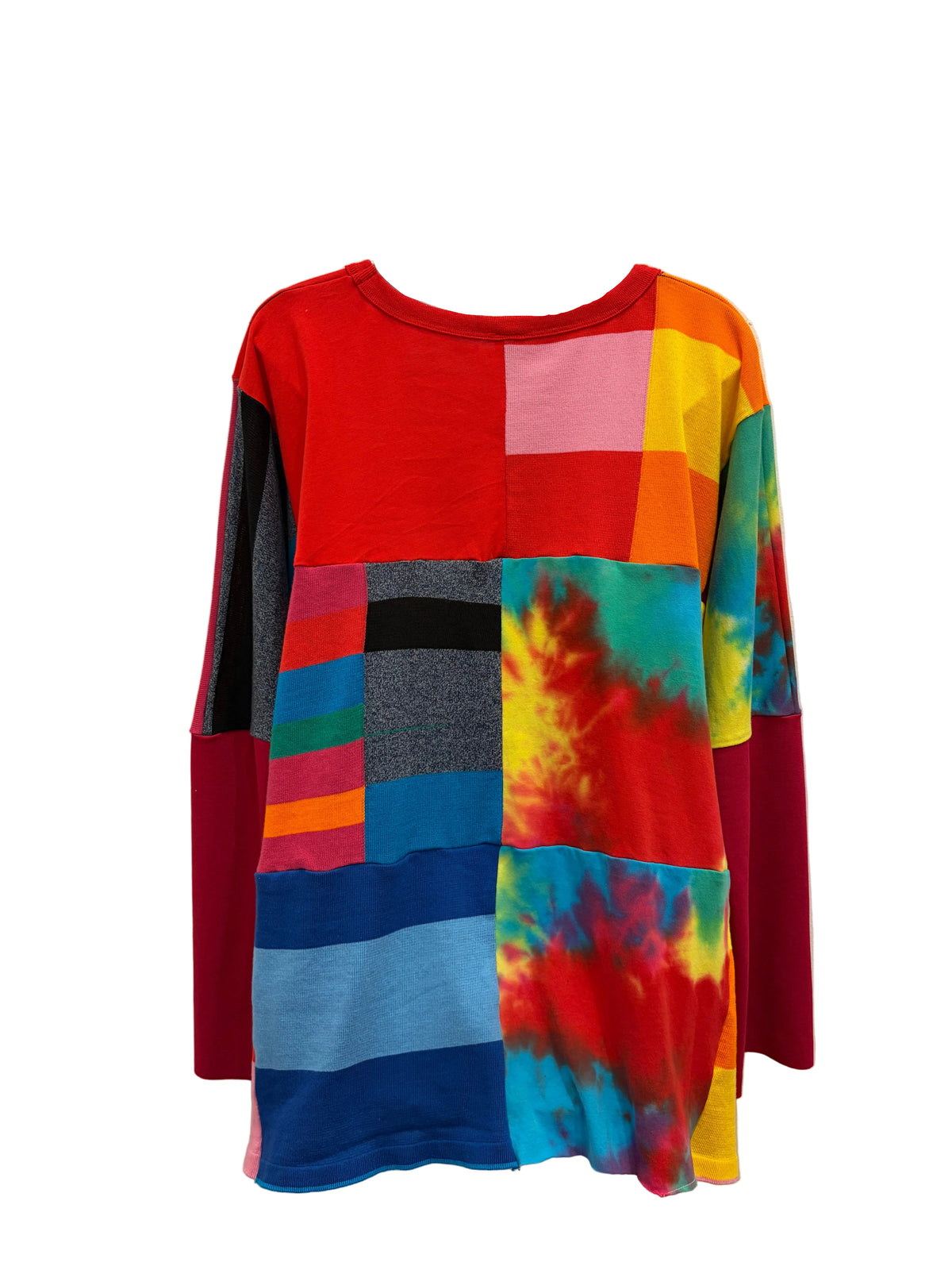 A long-sleeve patchwork knit top hanging on a clear plastic hanger against a plain beige wall. The shirt features a vibrant multicolor design with blocks of solid red, pink, yellow, orange, blue, gray, and tie-dye patterns.