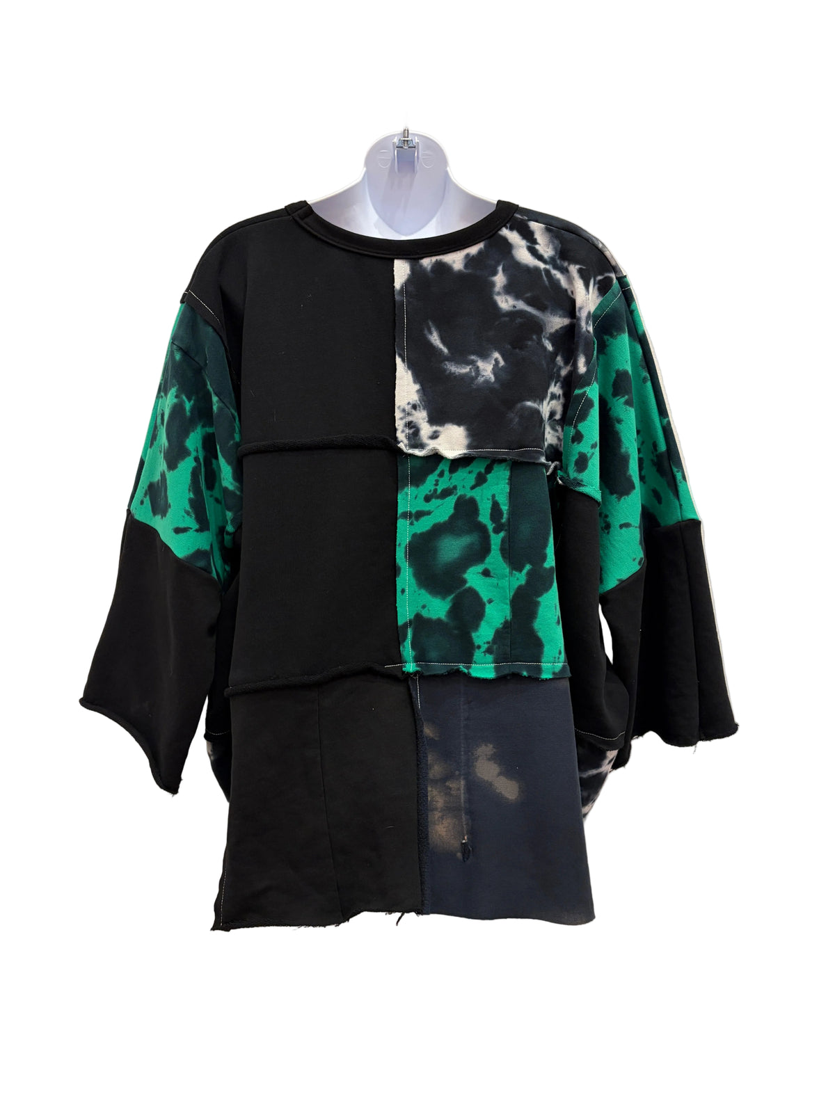A black patchwork sweatshirt with green and black tie-dye panels on the sleeves and chest, hanging on a clear plastic hanger.
