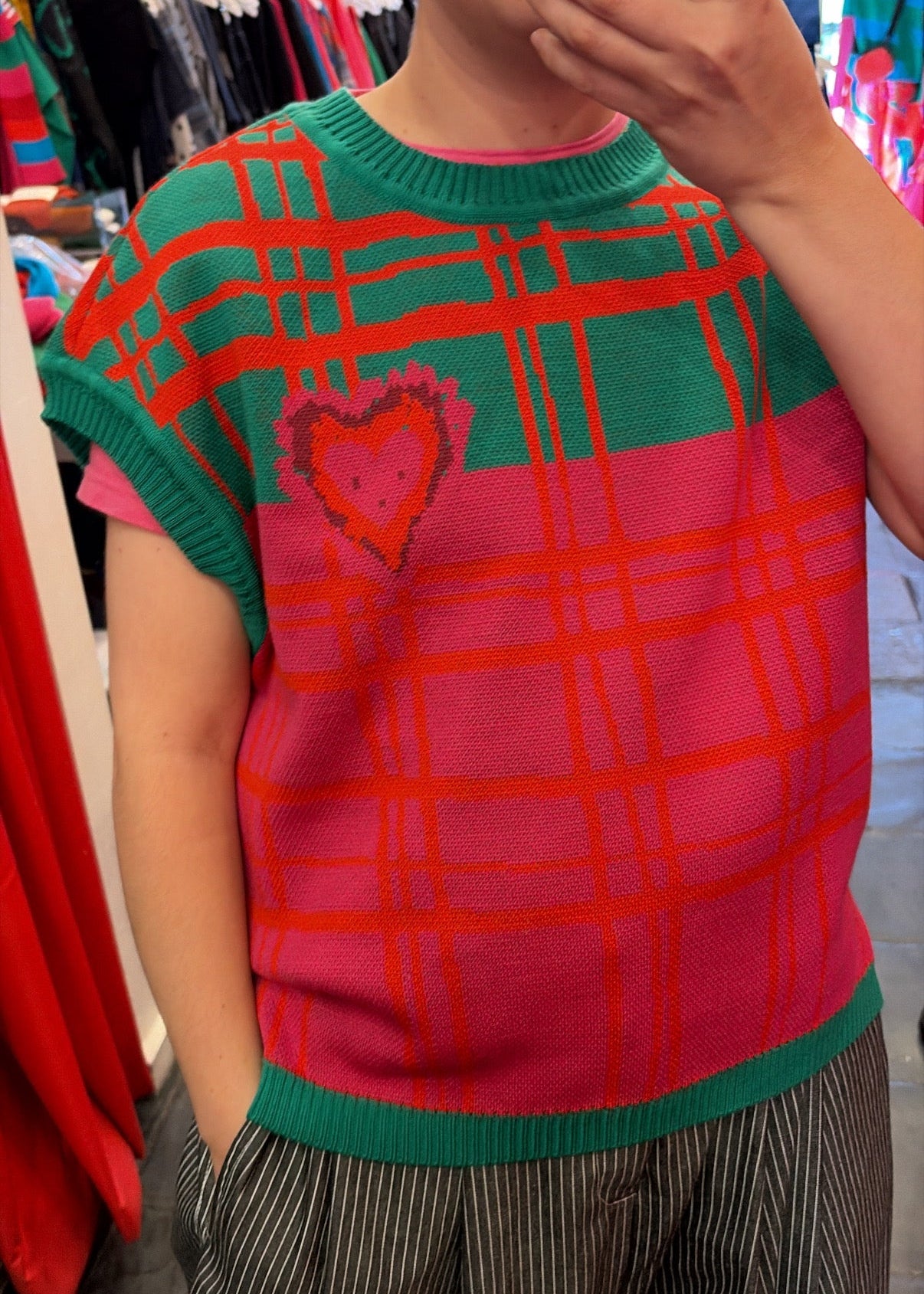 Person wearing a red and green checkered vest with a heart design in a clothing store.