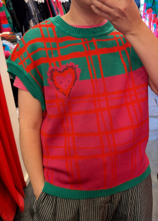 Person wearing a red and green checkered vest with a heart design in a clothing store.